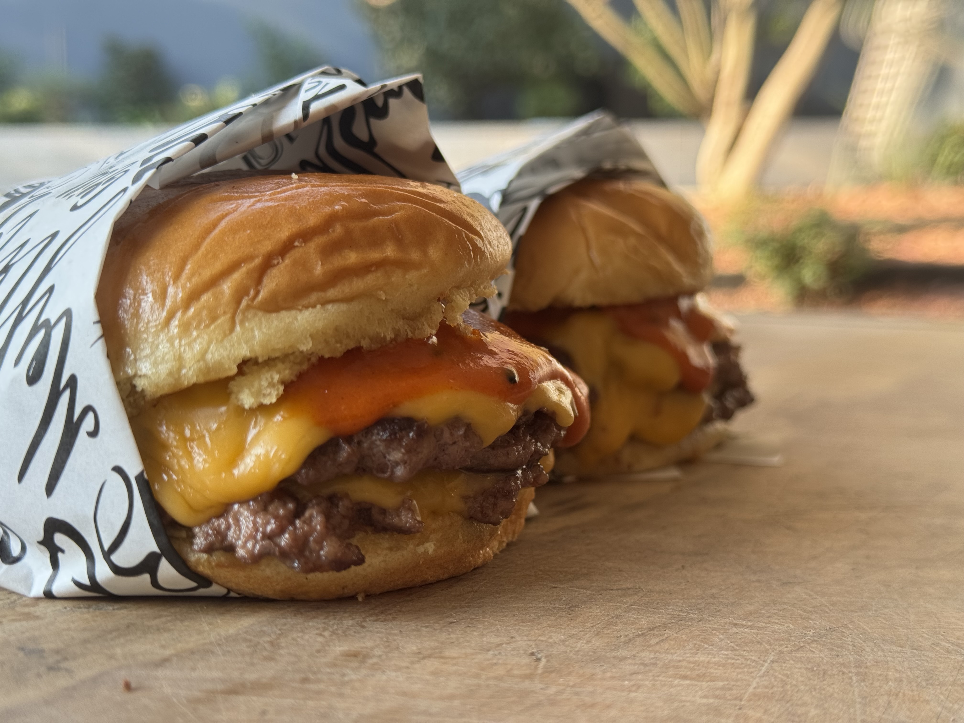 Dos hamburguesas smash envueltas en papel de marca con queso cheddar y salsas